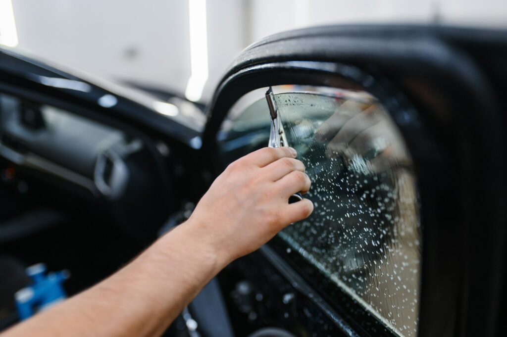 Male worker with squeegee wipes car tinting